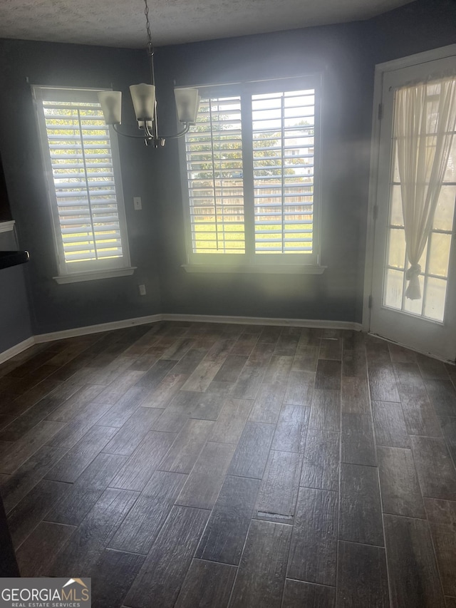 unfurnished dining area featuring dark wood-type flooring, a wealth of natural light, and a chandelier