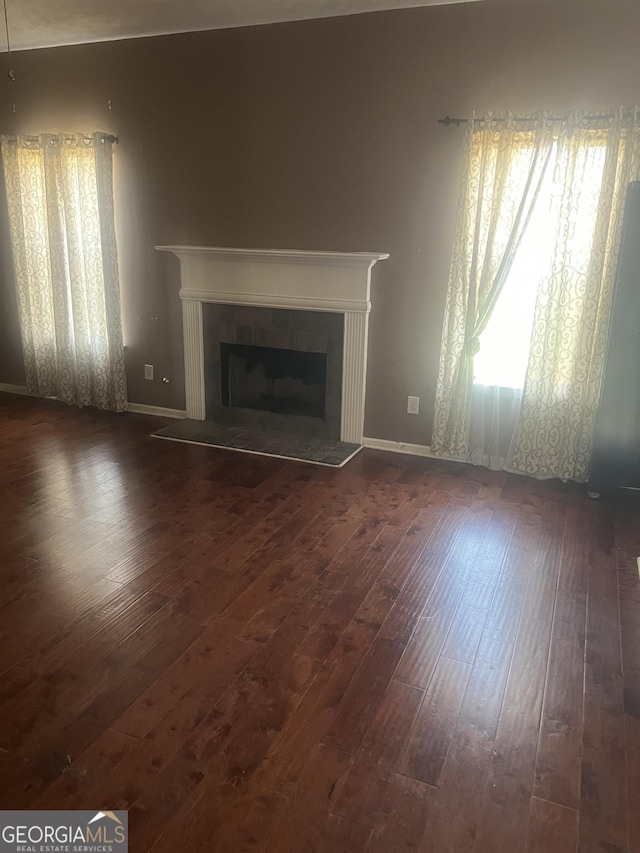 unfurnished living room featuring dark wood-type flooring and a tiled fireplace