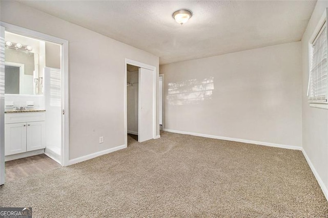 unfurnished bedroom with ensuite bathroom, a closet, light colored carpet, and sink