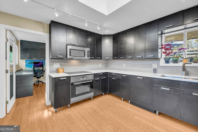 kitchen featuring tasteful backsplash, sink, light wood-type flooring, and appliances with stainless steel finishes