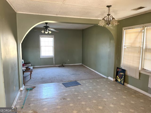 interior space with ceiling fan with notable chandelier, ornamental molding, and carpet