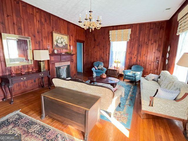 living room with wood-type flooring, ornamental molding, a notable chandelier, a brick fireplace, and a textured ceiling