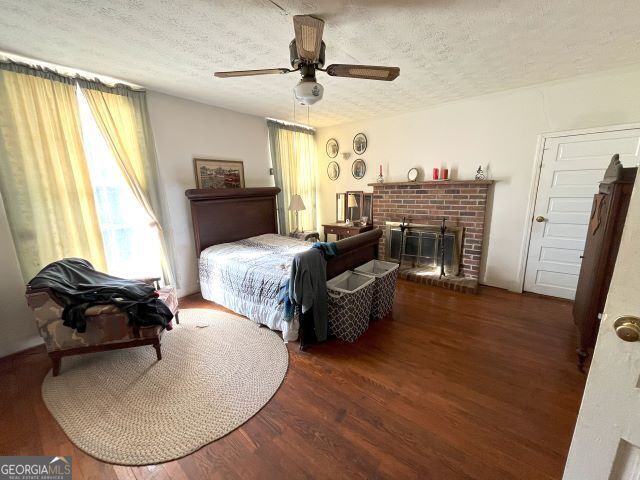 bedroom with ceiling fan, dark hardwood / wood-style flooring, a textured ceiling, and a fireplace