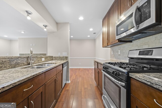 kitchen with light stone countertops, light wood-type flooring, stainless steel appliances, and sink