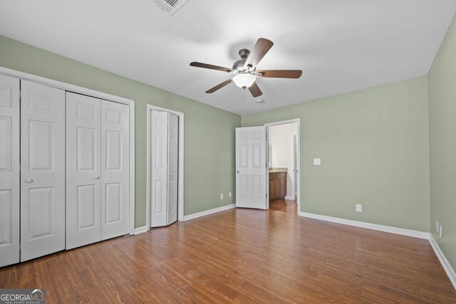 unfurnished bedroom with wood-type flooring, two closets, and ceiling fan