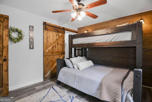 bedroom with a barn door, dark hardwood / wood-style floors, ceiling fan, and wood walls