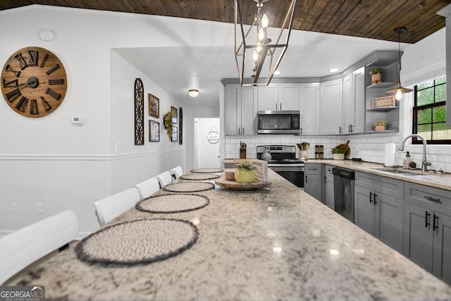 kitchen with light stone countertops, appliances with stainless steel finishes, gray cabinetry, sink, and hanging light fixtures