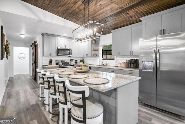 kitchen with a center island, hanging light fixtures, a barn door, wood ceiling, and appliances with stainless steel finishes