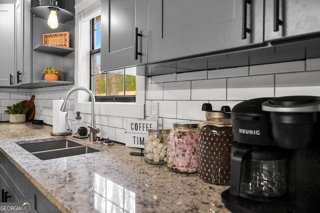 kitchen with tasteful backsplash, light stone counters, gray cabinetry, and sink