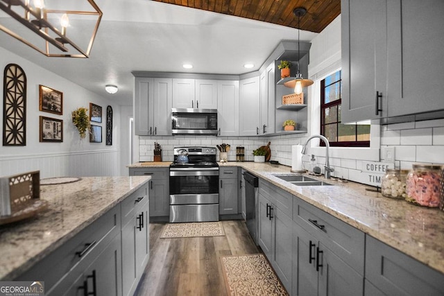 kitchen featuring gray cabinetry, hardwood / wood-style floors, sink, appliances with stainless steel finishes, and light stone counters