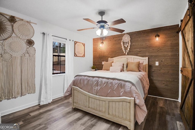 bedroom featuring dark hardwood / wood-style flooring, a barn door, ceiling fan, and wooden walls