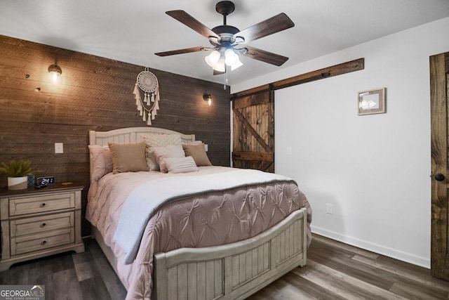 bedroom with ceiling fan, a barn door, dark wood-type flooring, and wooden walls