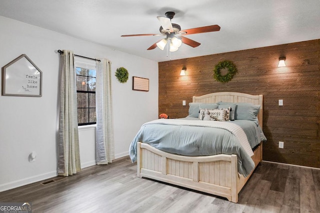 bedroom with wooden walls, ceiling fan, and wood-type flooring