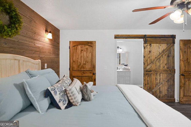 bedroom featuring a barn door, wood walls, ceiling fan, and ensuite bathroom