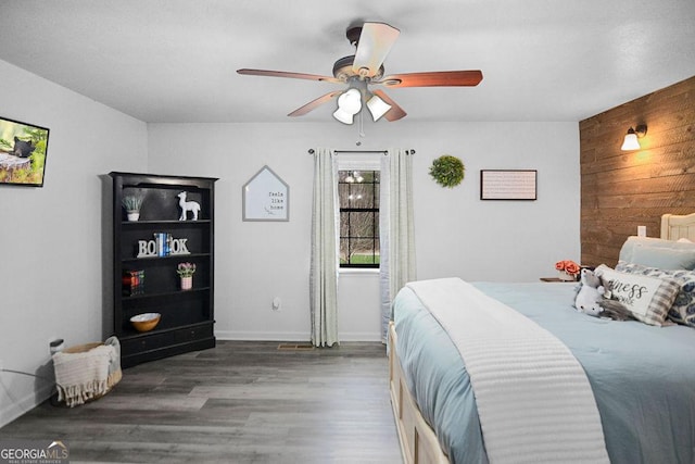 bedroom with ceiling fan, dark hardwood / wood-style flooring, and wooden walls