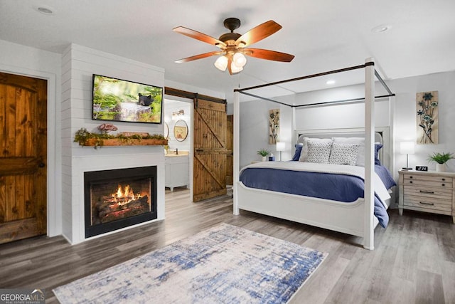 bedroom featuring hardwood / wood-style flooring, ceiling fan, a barn door, and a large fireplace