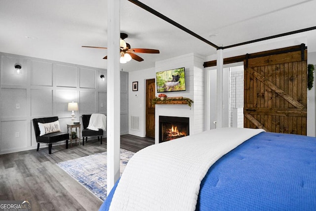 bedroom with hardwood / wood-style flooring, ceiling fan, a barn door, and a fireplace