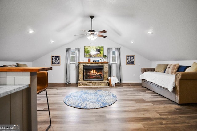 bedroom with a stone fireplace, ceiling fan, wood-type flooring, and vaulted ceiling