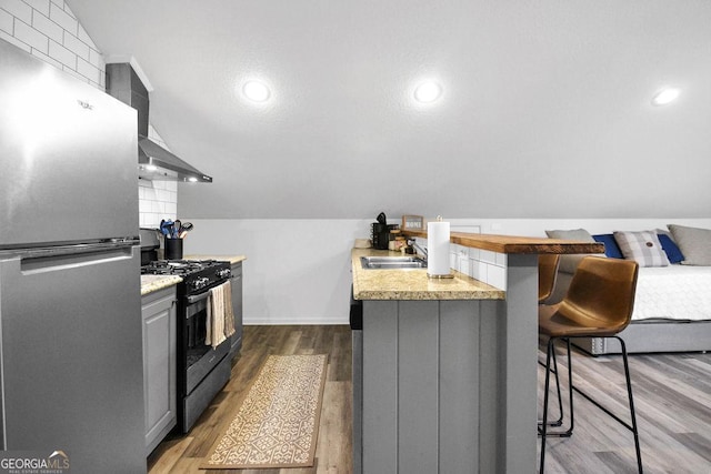 kitchen with appliances with stainless steel finishes, dark hardwood / wood-style flooring, gray cabinetry, vaulted ceiling, and a breakfast bar area