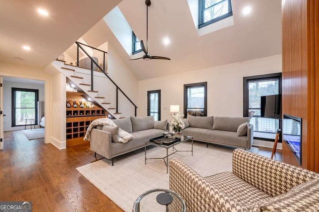 living room featuring ceiling fan, wood-type flooring, high vaulted ceiling, and a skylight