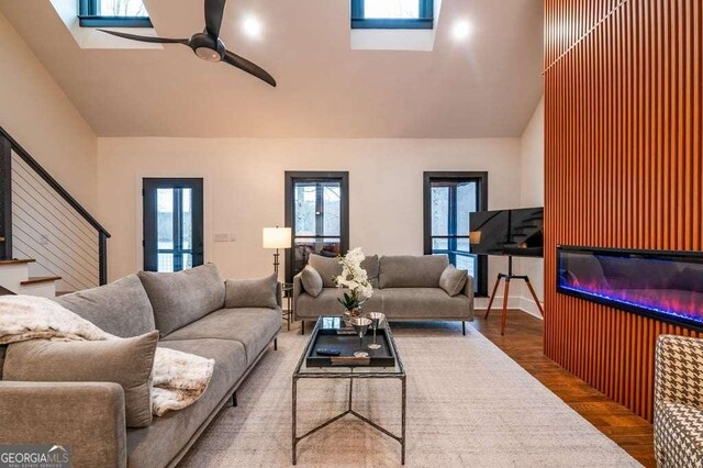 living room featuring ceiling fan, vaulted ceiling with skylight, and hardwood / wood-style flooring