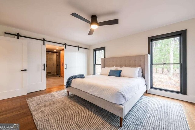 bedroom featuring a barn door, hardwood / wood-style flooring, and ceiling fan