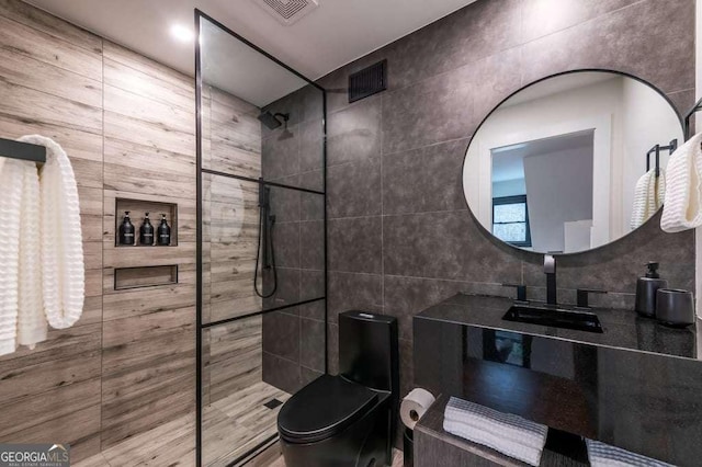 bathroom featuring tiled shower, toilet, tile walls, and sink