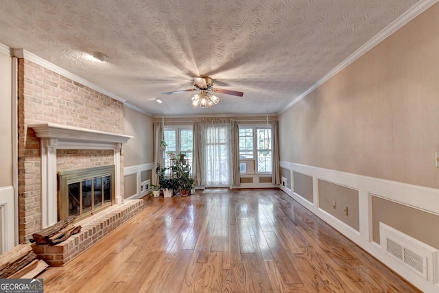 unfurnished living room with light wood-type flooring, a brick fireplace, ornamental molding, a textured ceiling, and ceiling fan