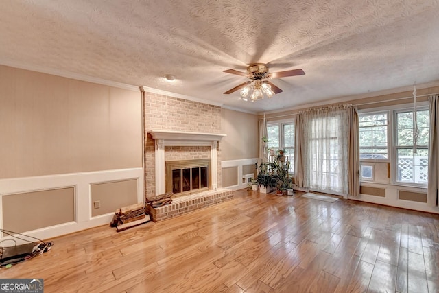 unfurnished living room featuring hardwood / wood-style flooring, ceiling fan, ornamental molding, and a brick fireplace