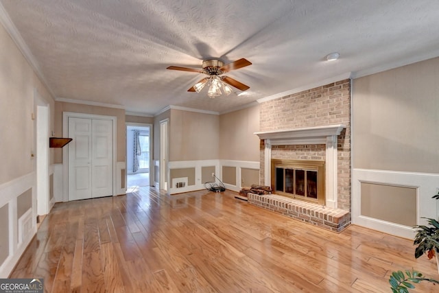 unfurnished living room featuring ceiling fan, a brick fireplace, crown molding, wood-type flooring, and a textured ceiling