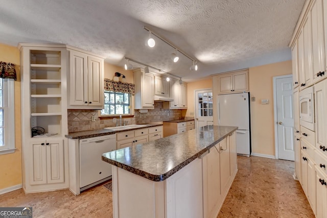 kitchen with a textured ceiling, white appliances, a kitchen island, and sink