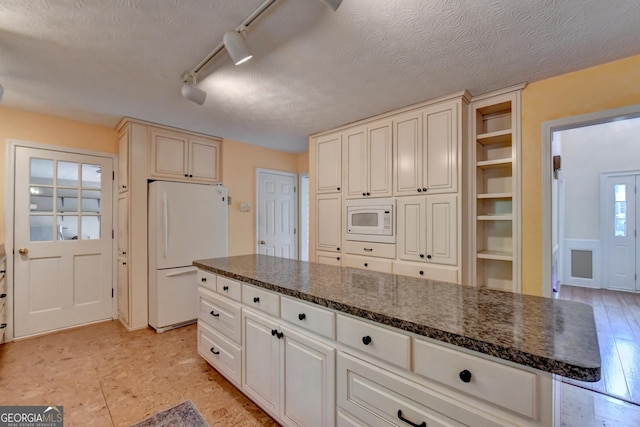 kitchen featuring a textured ceiling, white appliances, rail lighting, and dark stone countertops