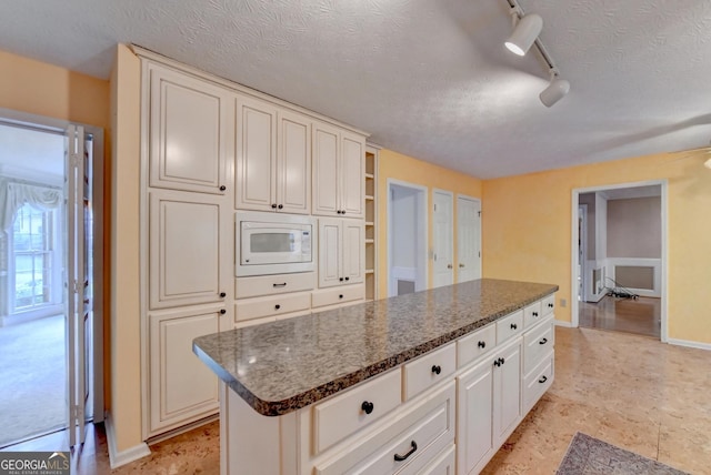 kitchen with a center island, white microwave, track lighting, dark stone countertops, and a textured ceiling