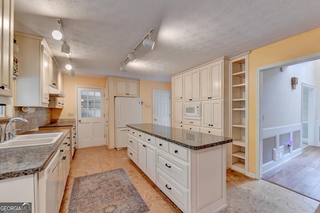 kitchen featuring rail lighting, white appliances, a textured ceiling, sink, and a center island