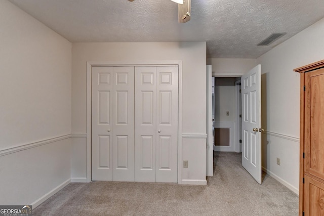 unfurnished bedroom with light carpet, a textured ceiling, a closet, and ceiling fan