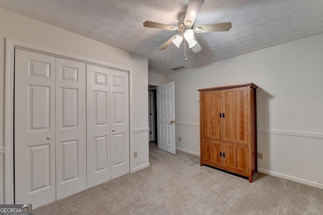 unfurnished bedroom with a textured ceiling, ceiling fan, light carpet, and a closet