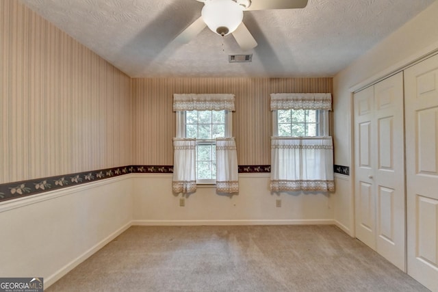 empty room featuring ceiling fan, a wealth of natural light, a textured ceiling, and light carpet