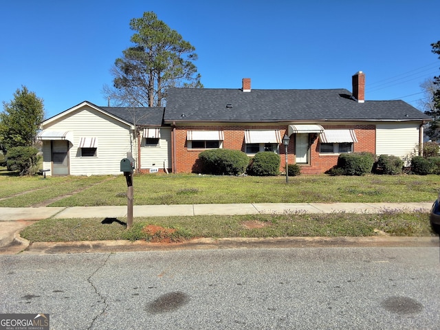 ranch-style home featuring roof with shingles, a front lawn, and brick siding