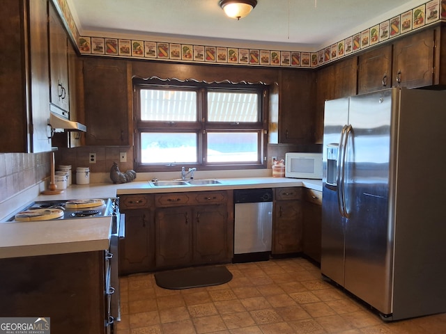 kitchen with under cabinet range hood, a sink, light countertops, appliances with stainless steel finishes, and dark brown cabinets