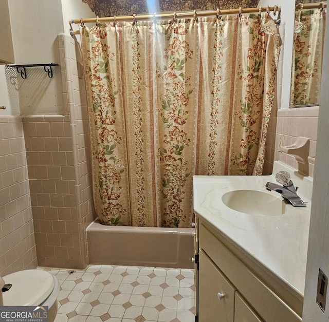 full bath with tile walls, toilet, shower / bath combo with shower curtain, wainscoting, and vanity