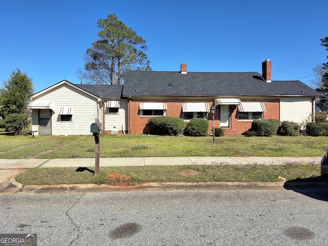 ranch-style house with a front lawn, roof with shingles, and brick siding