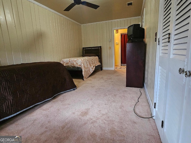 bedroom with ceiling fan, wooden walls, light colored carpet, visible vents, and crown molding