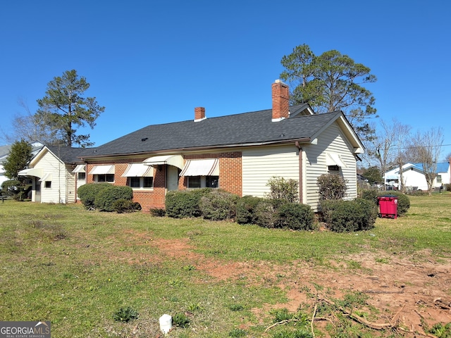 back of property with brick siding, a lawn, a chimney, and a shingled roof