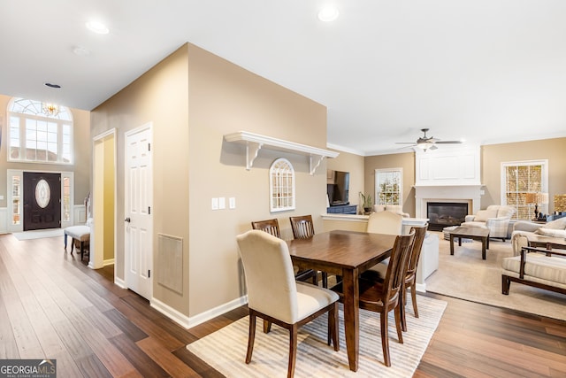 dining space with ceiling fan, a large fireplace, wood-type flooring, and a healthy amount of sunlight