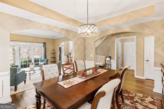 dining area with a raised ceiling, an inviting chandelier, ornamental molding, and dark wood-type flooring