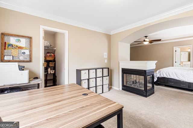 carpeted bedroom with ceiling fan, a multi sided fireplace, crown molding, a walk in closet, and a closet