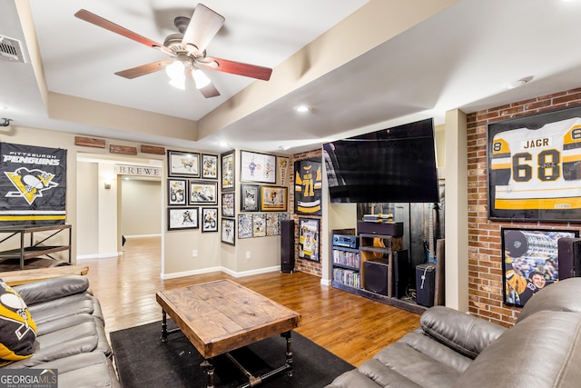 living room with a tray ceiling, ceiling fan, hardwood / wood-style floors, and brick wall