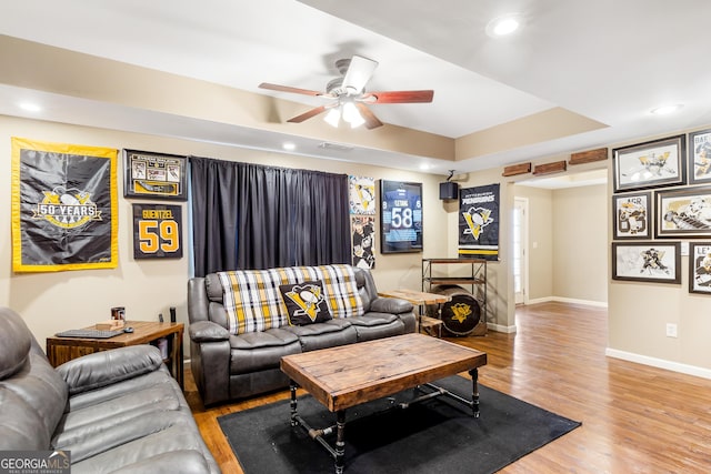 living room with a tray ceiling, ceiling fan, and light hardwood / wood-style flooring