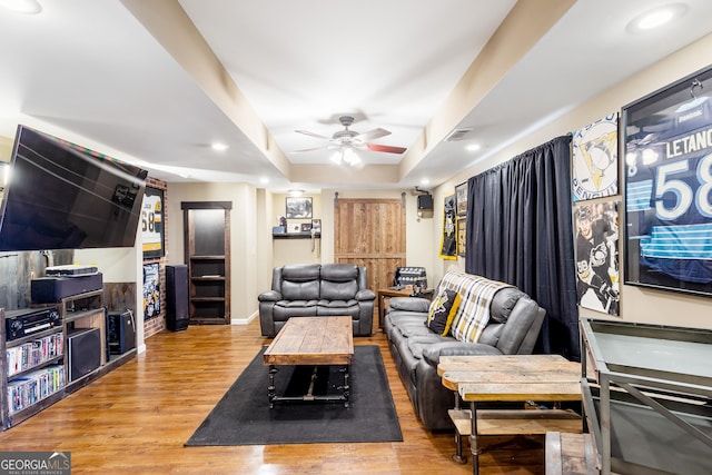 living room with ceiling fan, a raised ceiling, and wood-type flooring