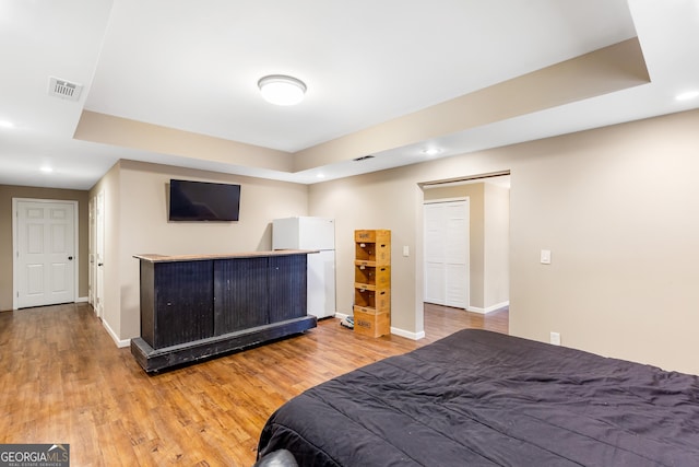 bedroom with hardwood / wood-style floors, white fridge, and a raised ceiling